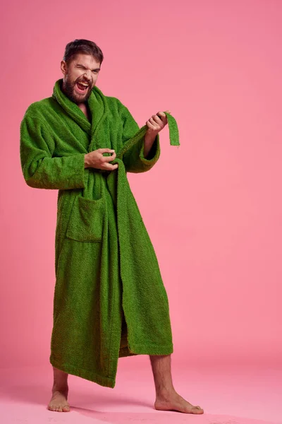 Um homem emocional em um manto verde em pleno crescimento em um fundo rosa gestos com as mãos para o modelo — Fotografia de Stock