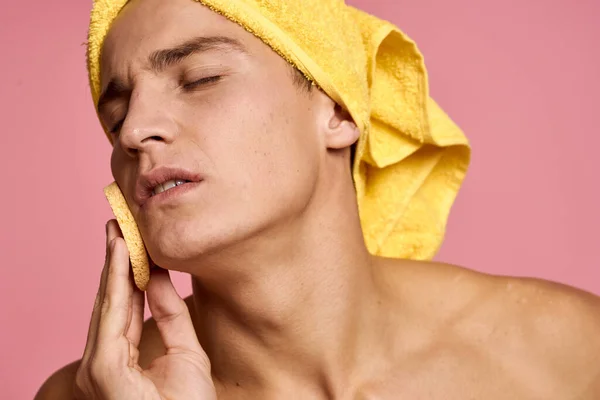 man with a towel on his head and a yellow sponge in his hand cosmetic procedure clean skin of the face