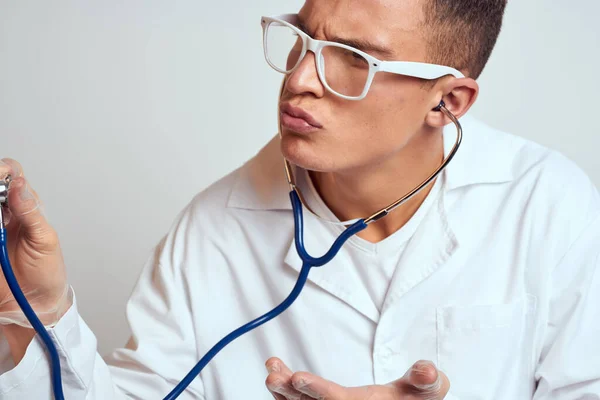 doctor in a medical gown with a stethoscope and glasses on a light background cropped view portrait