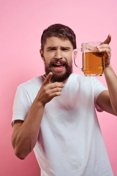 Homme barbu avec une tasse de bière Sur un fond rose émotions amusantes vue recadrée d'un T-shirt blanc ivre — Photo