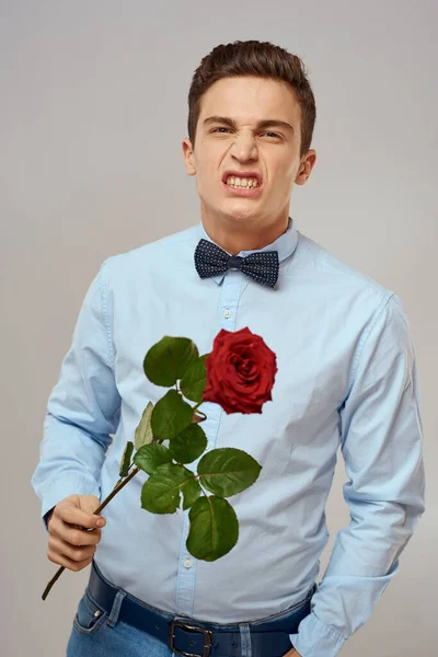 Romantikus férfi piros rózsával és kék ingben csokornyakkendővel a nyakában szürke háttér — Stock Fotó