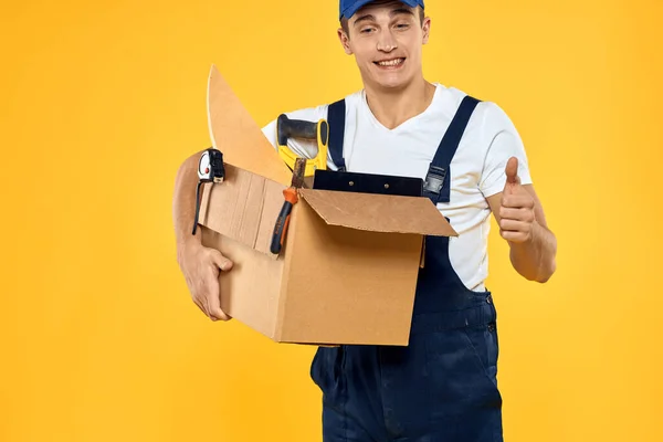 Trabalhador com caixa no carregador de ferramentas manuais fundo amarelo — Fotografia de Stock