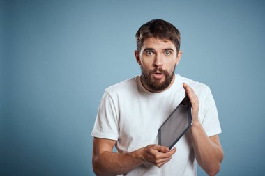 Beyaz tişörtlü, mavi arka planda dokunmatik tabletli enerjik bir adam.