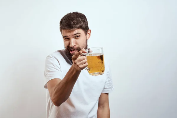 Homme avec une tasse de bière dans ses mains et un t-shirt blanc fond clair moustache barbe émotions modèle — Photo