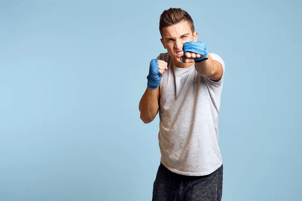 Sportovní muž v modrých boxerských rukavicích a tričku na modrém pozadí cvičení údery oříznutý pohled — Stock fotografie