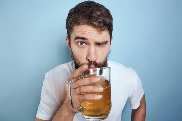Beyaz tişörtlü, bira kupalı, sarhoş, mavi arka planlı neşeli bir adam. — Stok fotoğraf