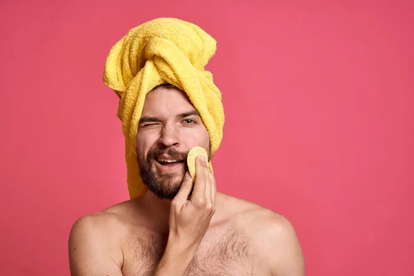 Man met blote schouders in een gele handdoek op zijn hoofd spons schone huid zorg roze achtergrond — Stockfoto