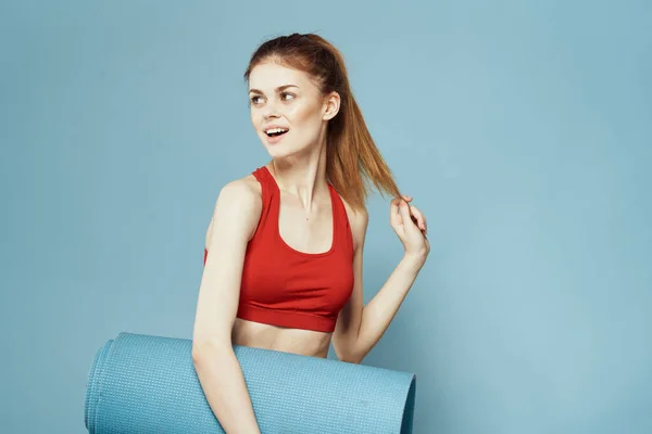 Sportos nő edzés szőnyeg kezekben Piros tank felső gyakorlat kék háttér — Stock Fotó