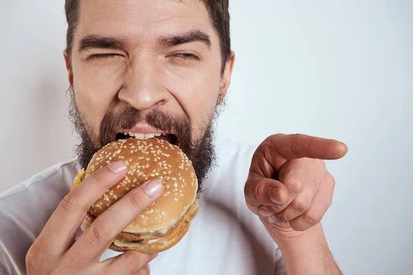 白いTシャツに身を包んだ男がハンバーガーを食べると、空腹のファーストフードが近くに見える — ストック写真