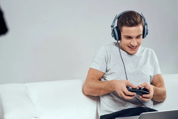 Muž na gauči před laptopem s joystickem ve sluchátkách videohry — Stock fotografie