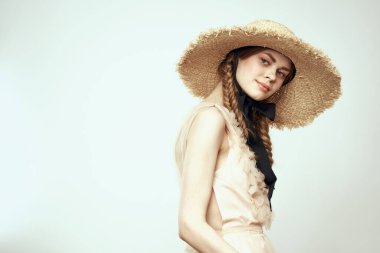 Hasır şapkalı, siyah kurdeleli ve arka planda açık bir elbise giyen hoş bir kız. Romantik bir model.