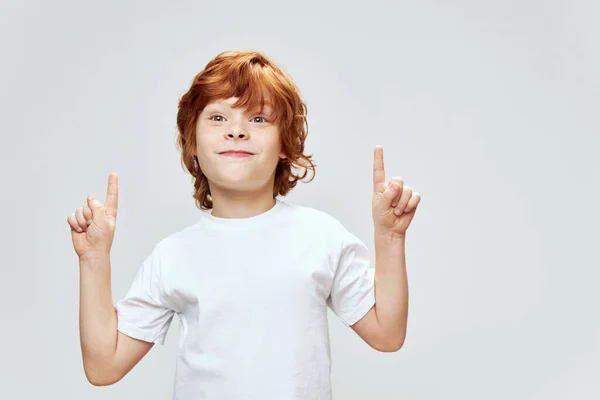 Menino alegre mostra duas mãos para cima com dedos de índice branco T-shirt corte vista — Fotografia de Stock