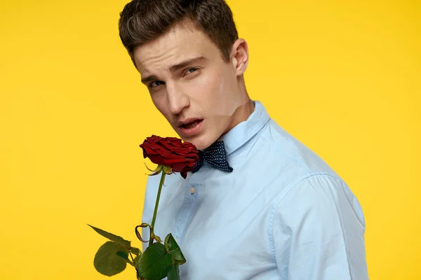 Retrato de un hombre con una rosa roja sobre un fondo amarillo y una camisa ligera pajarita caballero — Foto de Stock