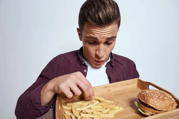 Homem comendo paletes de madeira fast food batatas fritas hambúrguer dieta comida restaurante luz fundo — Fotografia de Stock