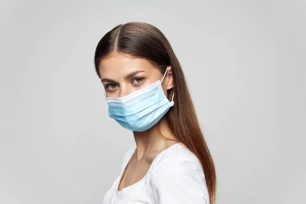 Hermosa chica en una máscara médica y en una camiseta blanca mira hacia adelante vista lateral aislado fondo — Foto de Stock