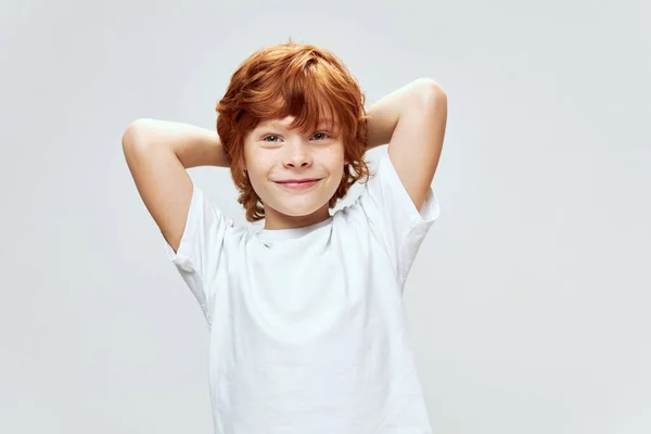 Alegre vermelho de cabelos menino de mãos dadas atrás de sua cabeça sorriso branco t-shirt — Fotografia de Stock