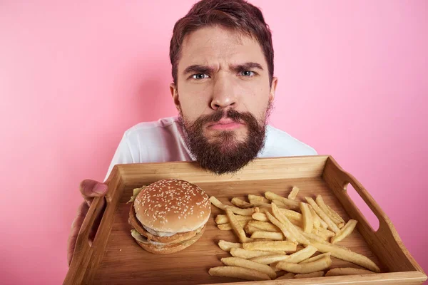 男で食べ物のトレイで彼の手ハンバーガーフライドポテトとファーストフードカロリーピンクの背景の肖像画クローズアップ — ストック写真