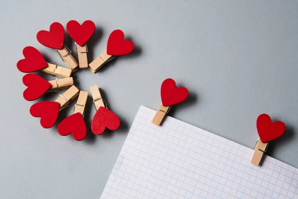 Kolíky v podobě srdíček na bílém listu papíru oříznutý pohled Valentines den dekorace — Stock fotografie