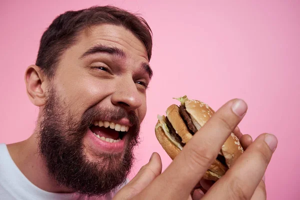 Retrato de um homem com um hambúrguer em um fundo rosa close-up vista recortada de um modelo — Fotografia de Stock