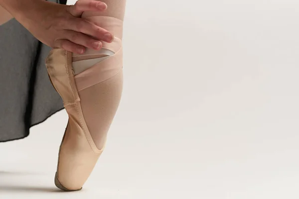 バレリーナは彼女の足の上にポイントシューズを置きますホワイトリボンモデルダンス光の背景. — ストック写真