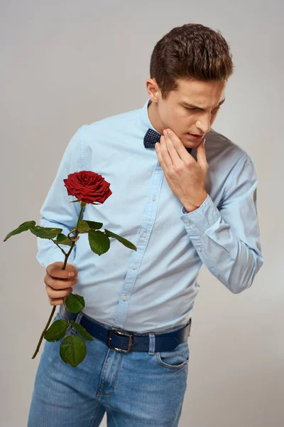 Handsome man with red rose blue shirt bow tie light background cropped view