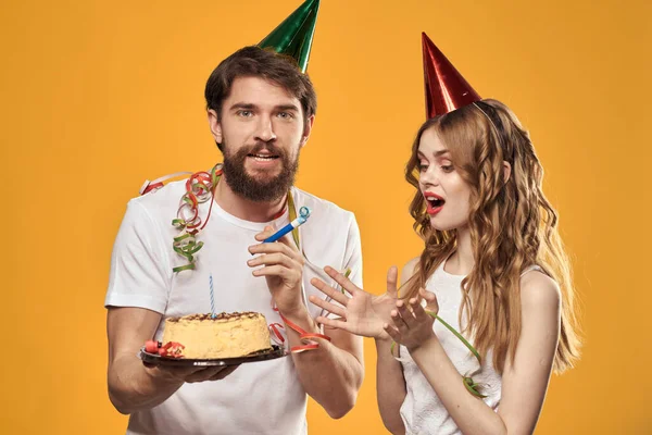 Šťastný muž a žena v čepici slaví narozeniny na žlutém pozadí s dort v rukou — Stock fotografie