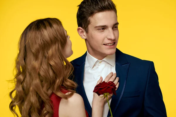 Романтик обнимает женщину в красном платье с розой в руке на жёлтом фоне — стоковое фото