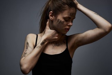 Gri arka planda kırıcı yazılar yazan üzgün kadın elleriyle kendine dokunuyor.