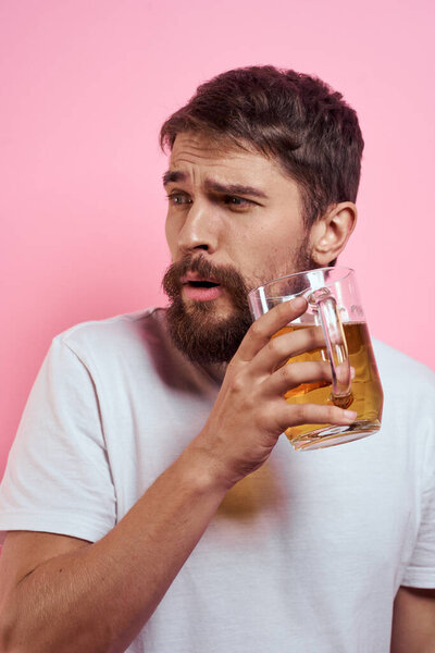 Bearded man with a mug of beer On a pink background fun emotions cropped view of a white T-shirt drunk