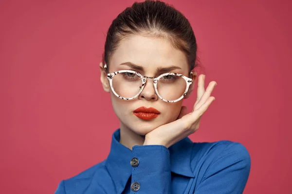 Porträtt av en kvinna i glasögon och i en blå skjorta röda läppar rosa bakgrund modell — Stockfoto