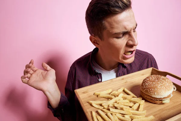 Hombre con comida rápida comer hamburguesa papas fritas fondo rosa — Foto de Stock