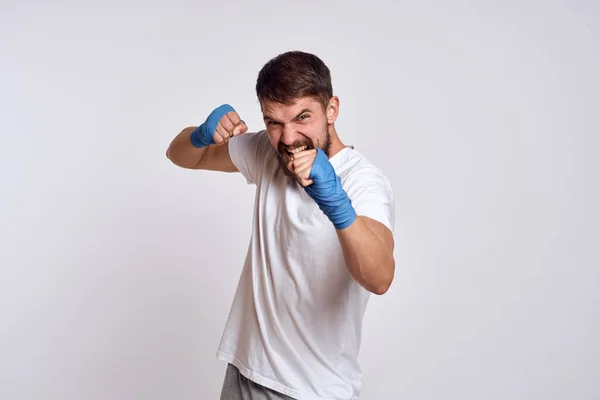 Hombre deportivo en camiseta blanca vendajes de boxeo azul en sus ejercicios de entrenamiento de brazos — Foto de Stock