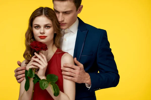 Milenci muži žena s červenou růží v rukou romantika dovolená žluté pozadí rodina přátelé. — Stock fotografie