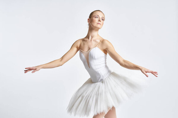 Ballerina in a white tutu performing dance exercise on light background. High quality photo