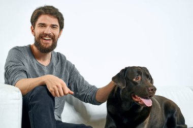 Beyaz bir kanepede siyah köpeği olan bir adam. Arka planda, yakın planda kesilen evcil hayvan insan arkadaş duyguları. Eğlenceli.