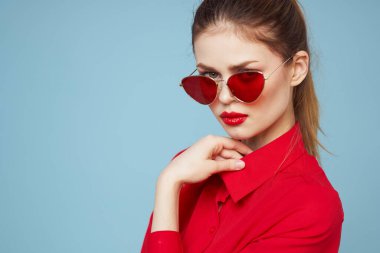 Koyu renk gözlüklü, kırmızı gömlekli, parlak makyajlı çekici bir kadın.