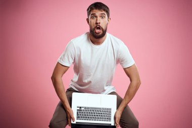 Açık dizüstü bilgisayarı olan beyaz tişörtlü bir adam elleri kırpılmış yeni teknoloji klavye monitörüyle jest yapıyor.