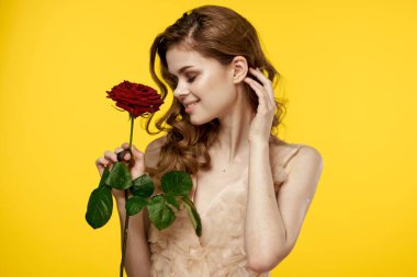 Sarı arka planda, elinde kırmızı bir çiçek ve gece elbisesi modeliyle romantik bir kız.