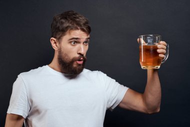 Elinde bir kupa birayla gezen bir adam duyguları olan eğlenceli bir yaşam tarzı beyaz tişört koyu tenha bir arka plan.