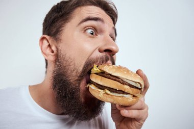Beyaz bir tişörtle arka planda hamburger yiyen bir adam yakın çekim açlık ve fast food manzarası izledi.