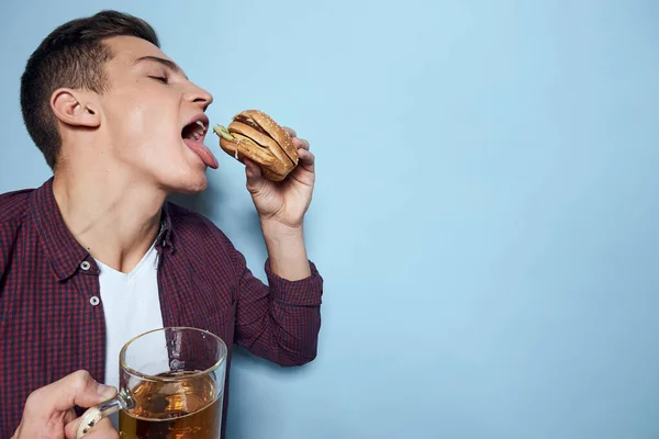 Alegre borracho hombre con cerveza taza y hamburguesa en mano dieta comida estilo de vida azul fondo — Foto de Stock