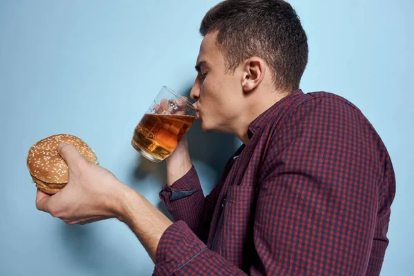 Alegre borracho hombre con cerveza taza y hamburguesa en mano dieta comida estilo de vida azul fondo —  Fotos de Stock