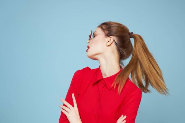 Koyu renk gözlüklü, kırmızı dudaklı, cazibeli stüdyo mavi arka planlı bir kadın.