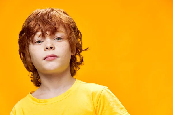 Red-haired boy looking ahead on yellow isolated background cropped view