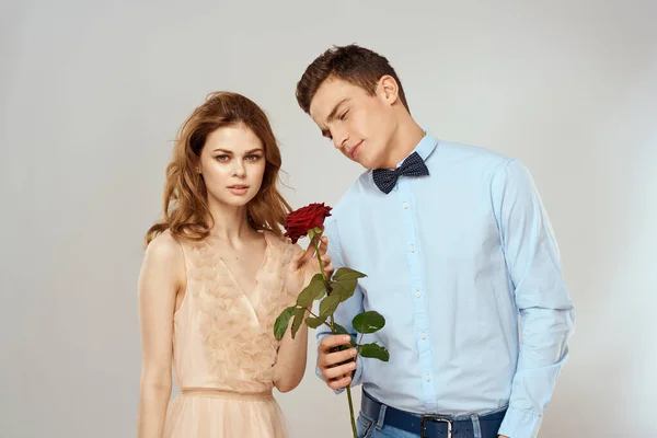 Una pareja joven y cariñosa con una rosa roja en sus manos en un romance de fondo claro —  Fotos de Stock