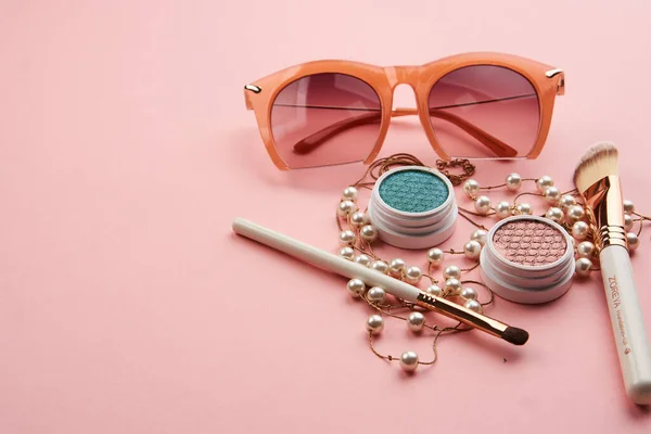 Óculos acessórios contas maquiagem pincéis coleção cosméticos profissionais em fundo rosa — Fotografia de Stock