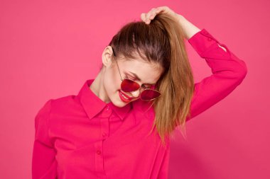 Güneş gözlüklü, elleri ve pembe gömlekli, saçlarına dokunan neşeli bir kadın.