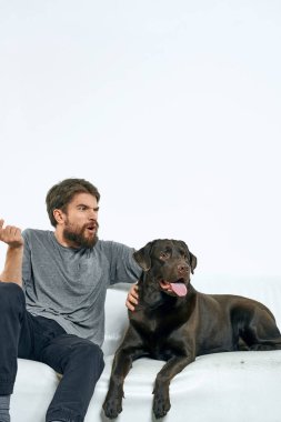 Beyaz bir kanepede siyah köpeği olan bir adam. Arka planda, yakın planda kesilen evcil hayvan insan arkadaş duyguları. Eğlenceli.