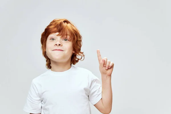 Рудоволоса дитина показує індексний палець вгору біла футболка обрізаний вид на сірий фон Копіювати простір — стокове фото