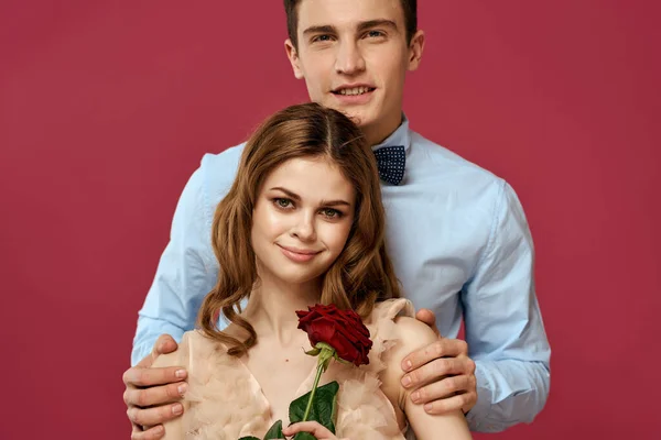 Verliebte Männer und Frauen mit einer roten Blume auf rosa Hintergrund umarmen sich. — Stockfoto